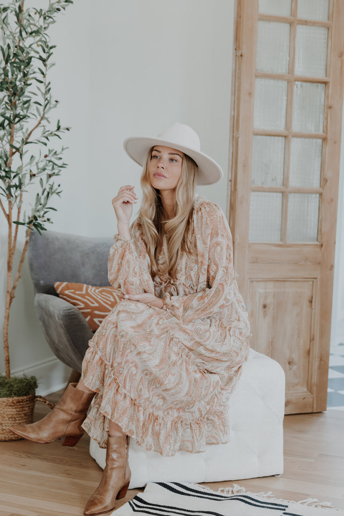 model wearing paisley printed boho maxi dress with ivory wide brim hat and cognac leather ankle boots sitting down - Hudson Blake - Downtown Greenville, SC