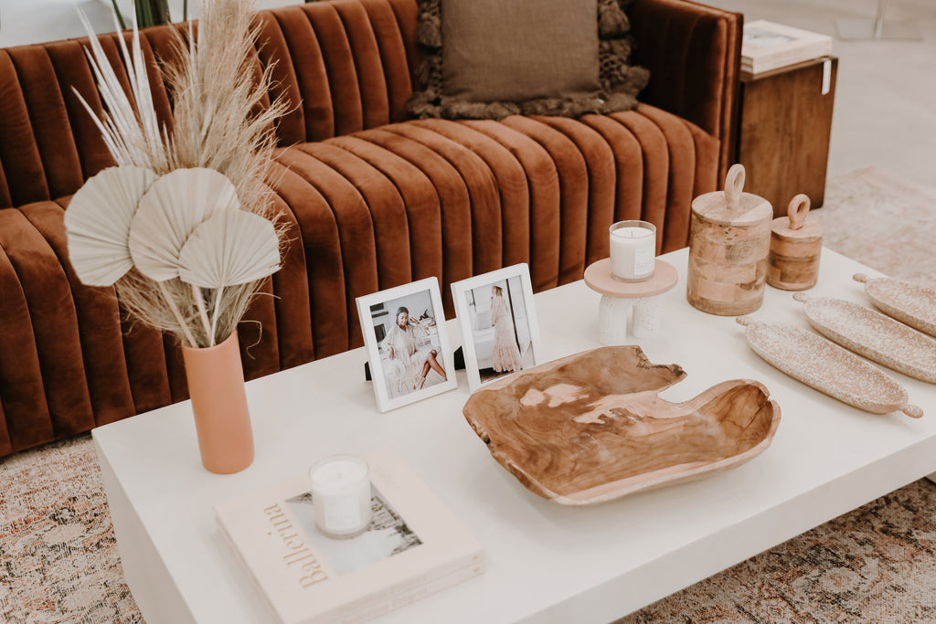 rust velvet sofa with sleek modern white concrete coffee table with vintage-inspired heirloom-quality decor accessories, coffee table accessories, wooden bowl, ceramic terracotta vase, terrazzo bowls, wooden canisters with lids, curve ceramic stand, coffee table books, lololi rug