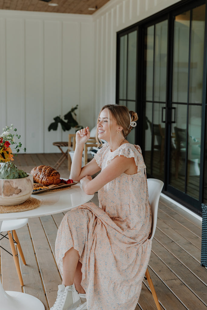 model sitting at a table wearing a tiered floral blush pink maxi dress with ruffle sleeve detail and a trendy hair clip | Hudson Blake lifestyle and home | shophudsonblake.com
