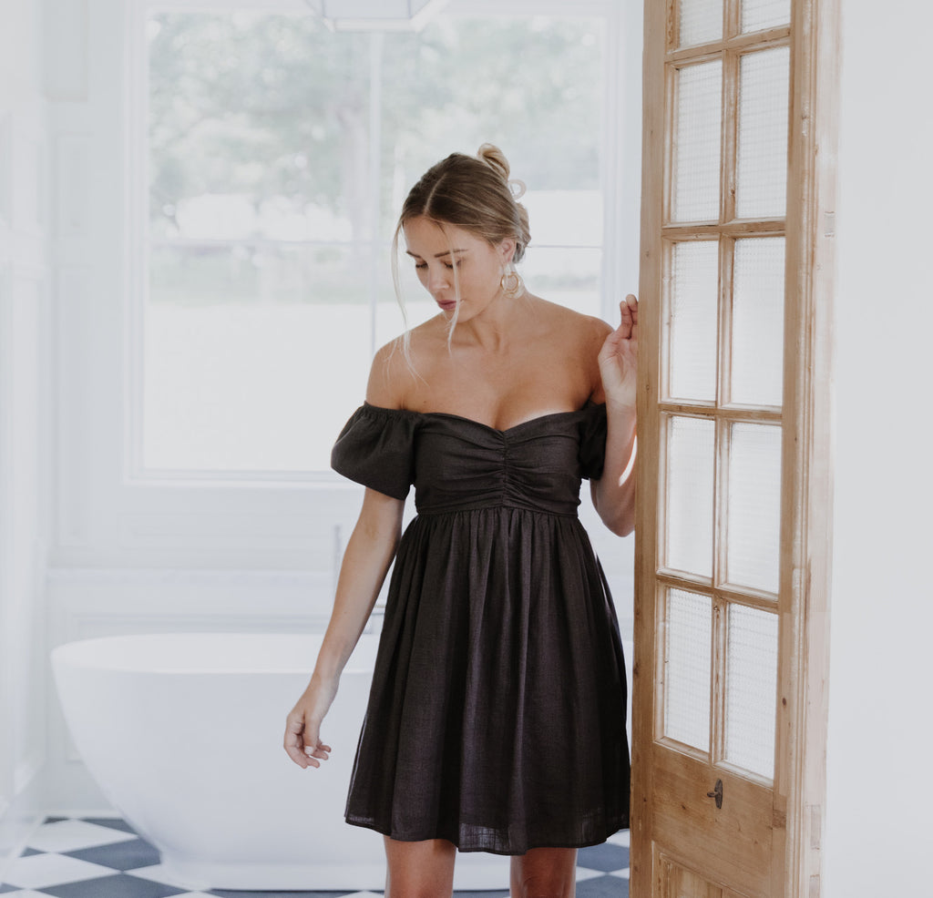 model standing in doorway wearing charcoal grey off-the-shoulder babydoll dress with cognac tan ankle boots and hair up in trendy hair clip | Hudson Blake lifestyle and home | shophudsonblake.com